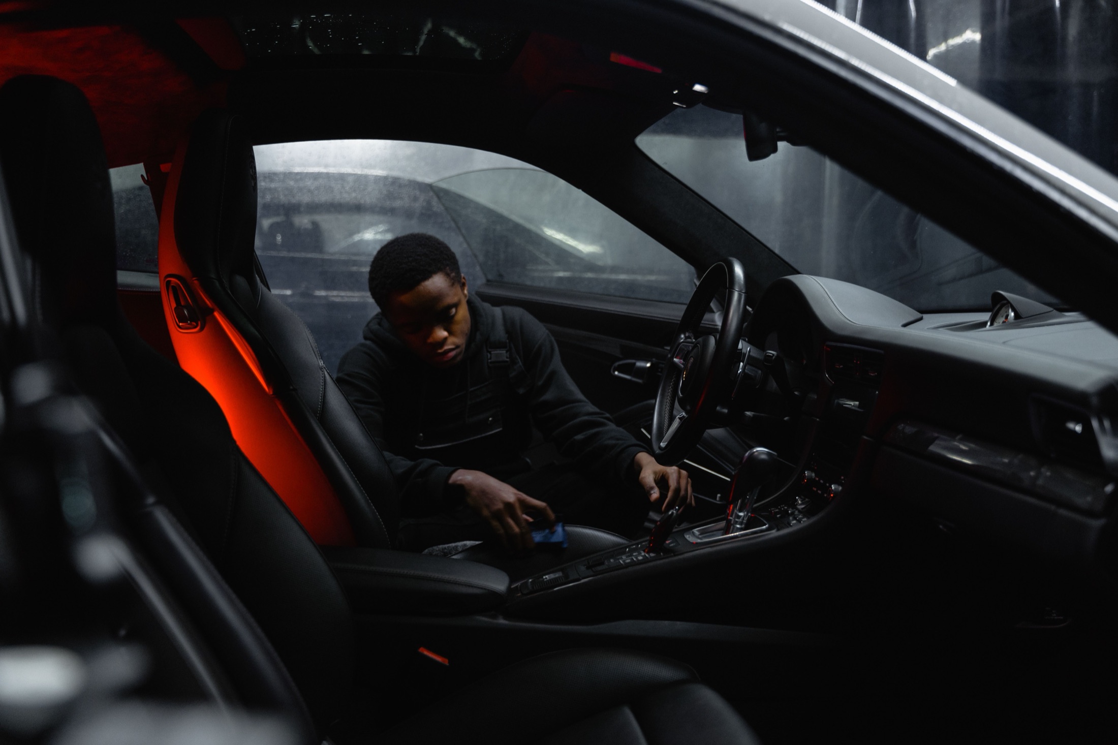 A detailer cleaning a dark vehicle interior by hand